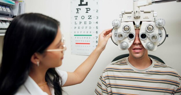 An optometrist adjusts a phoropter while a patient reads an eye chart during an eye exam.