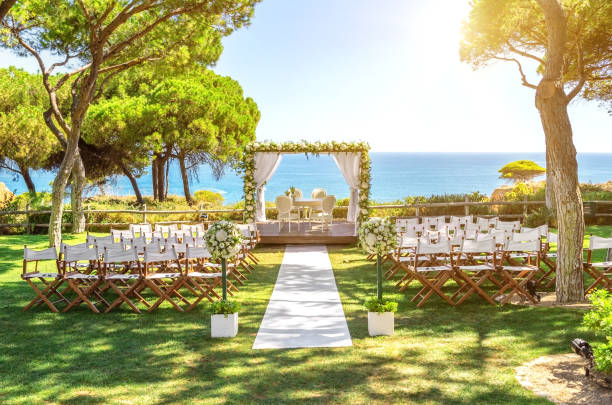 Outdoor wedding ceremony setup with white chairs, floral decorations, and an aisle leading to an altar overlooking the ocean.