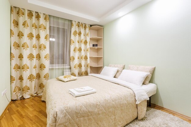 Modern bedroom with large bed, soft bedding, bedside lamp, wooden nightstand, and floor-to-ceiling curtains.