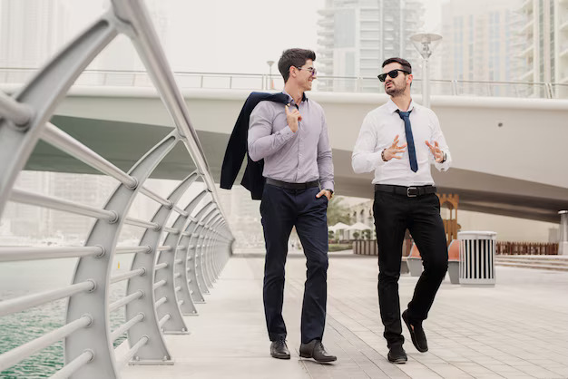 Two businessmen walking and talking on a modern waterfront promenade in business attire.

